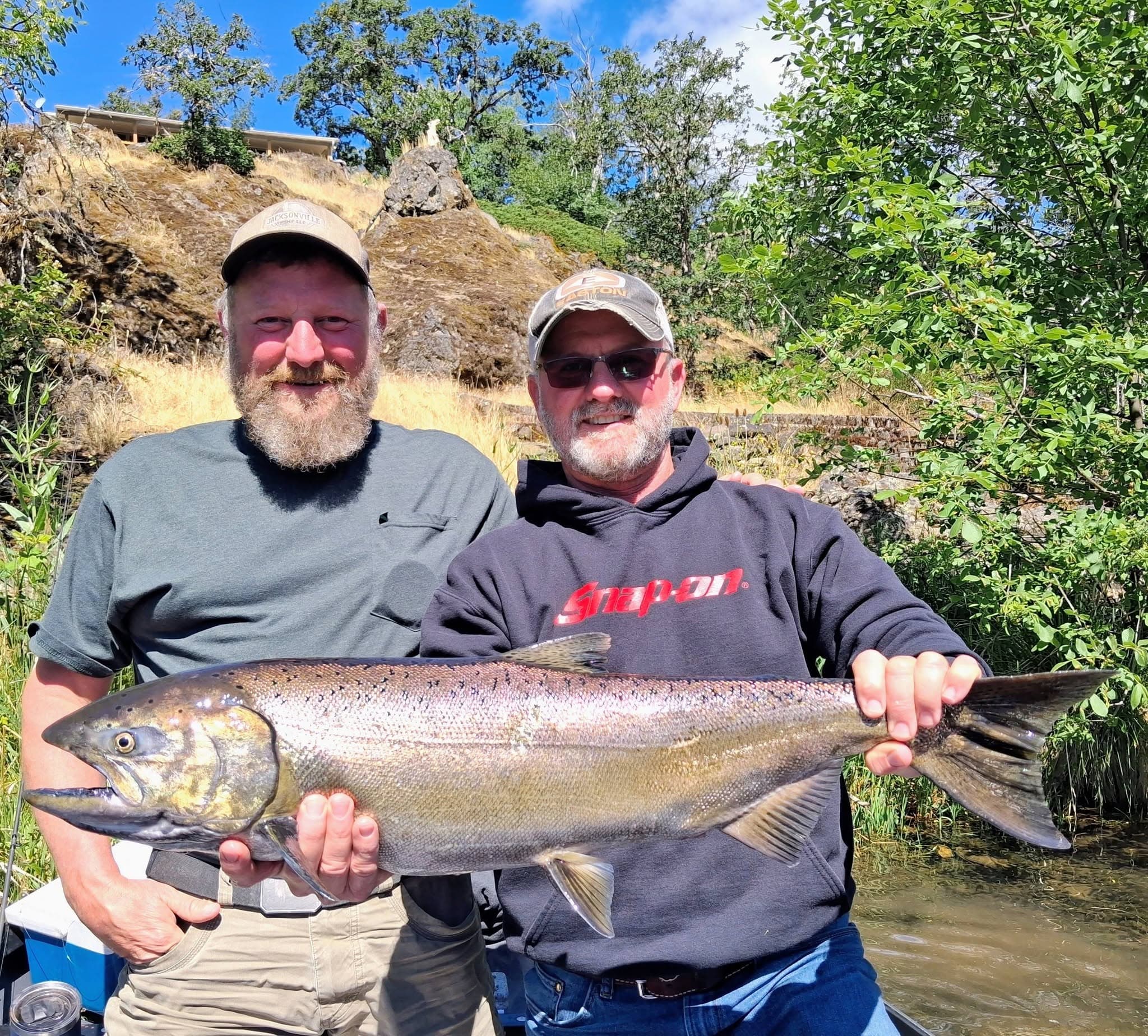 Two anglers holding a bright Chinook salmon on the river
